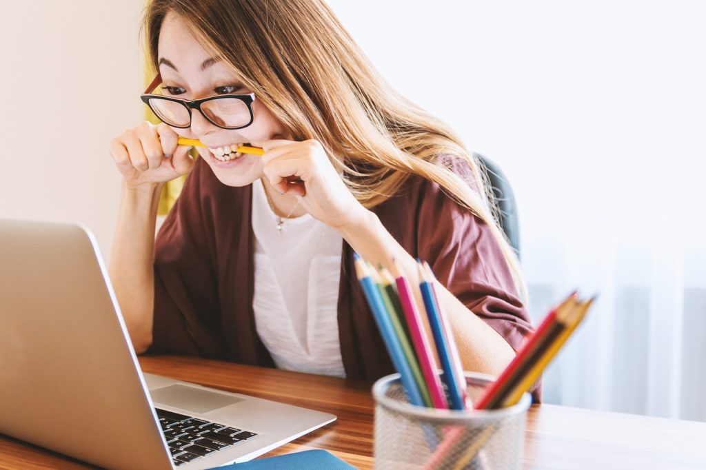 Moça ansiosa olhando a tela do computador e mordendo um lápis.